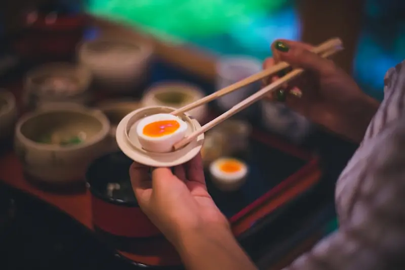 A woman is holding a boiled egg with chopsticks | Best Cooking Classes in Japan