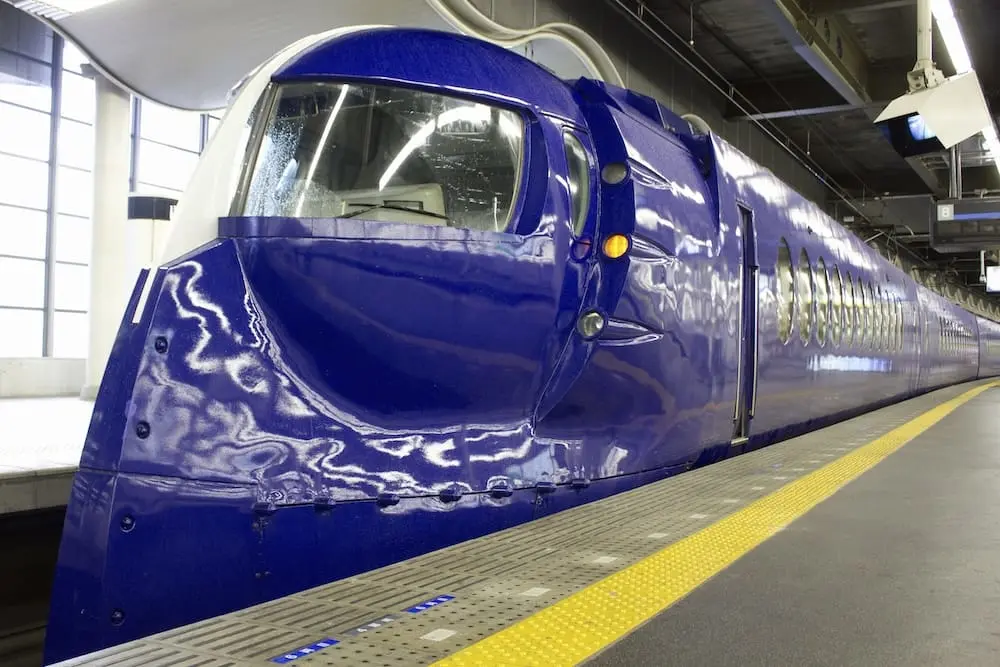 The bright blue Nankai Rapi:t Express Train arriving at the yellow-lined platform of Namba Station, with a reflective sheen on the train's front area and mist forming on the windows.