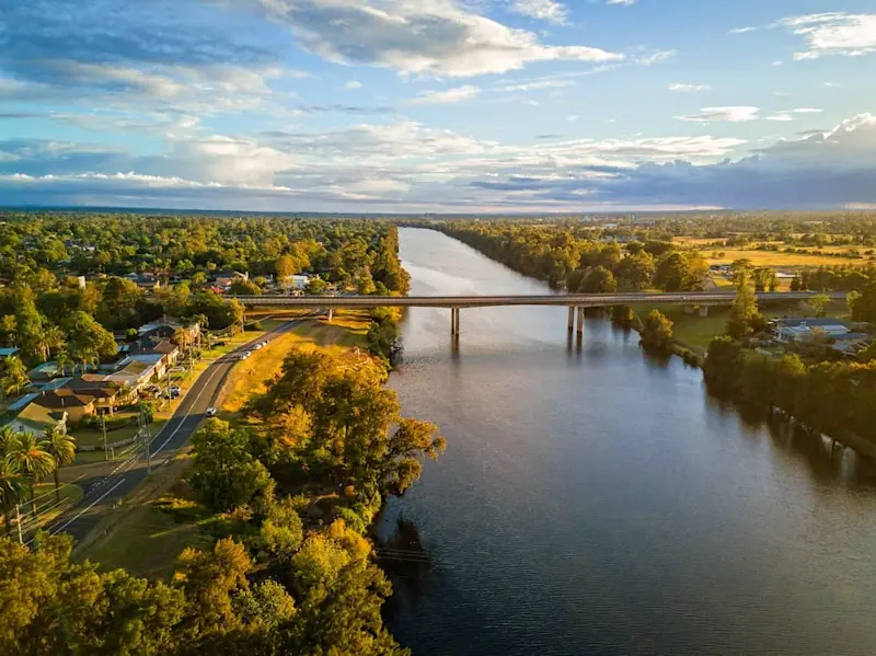 Aerial view of the Nepean River in Penrith, Western Sydney, at sunset, casting a golden glow over the roads and trees, with the M4 bridge crossing the river in the foreground.