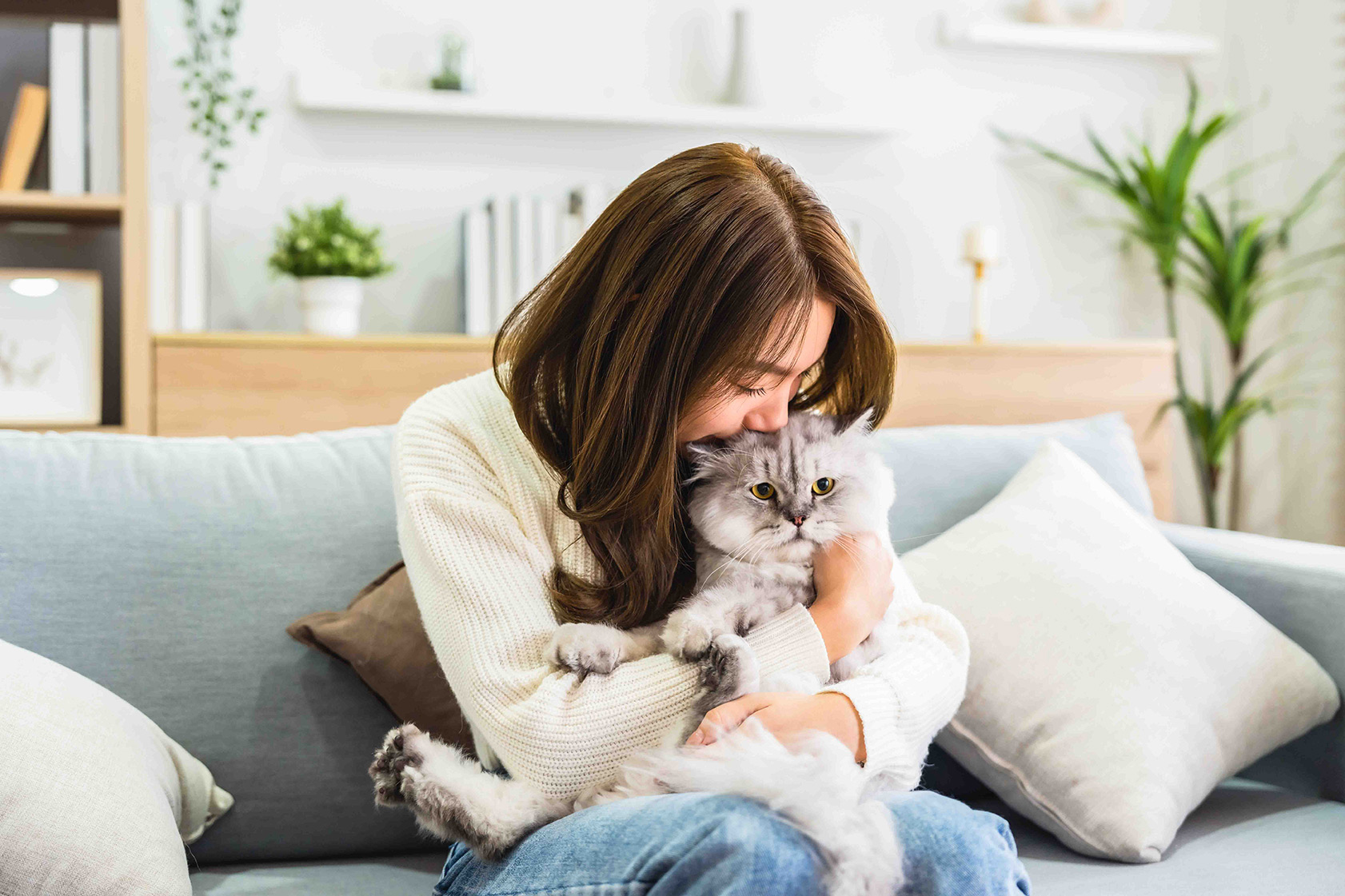 A woman sitting inside on a sofa while hugging her cat.