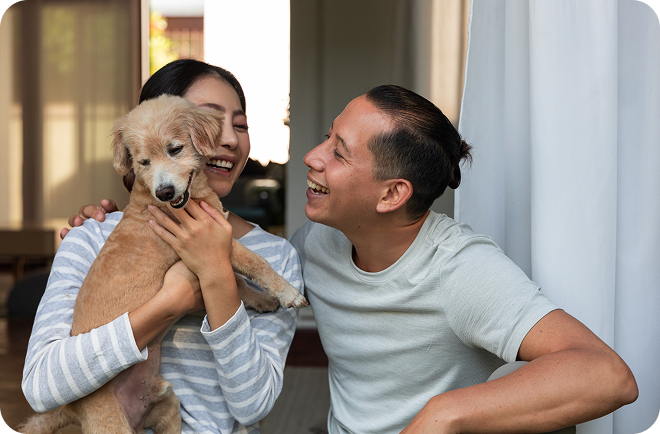 Person in yellow shirt hugging a black dog outdoors in a grassy field