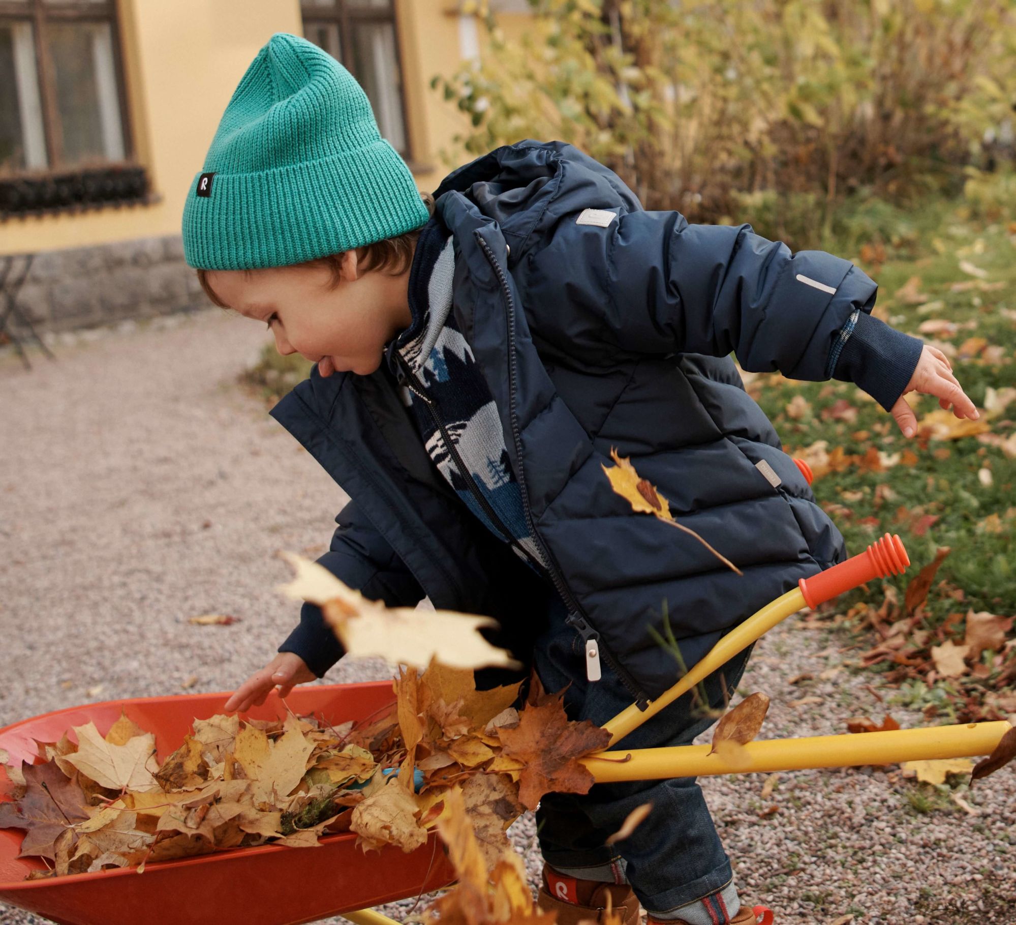 Barn krattar löv i en reima jacka från babyshop