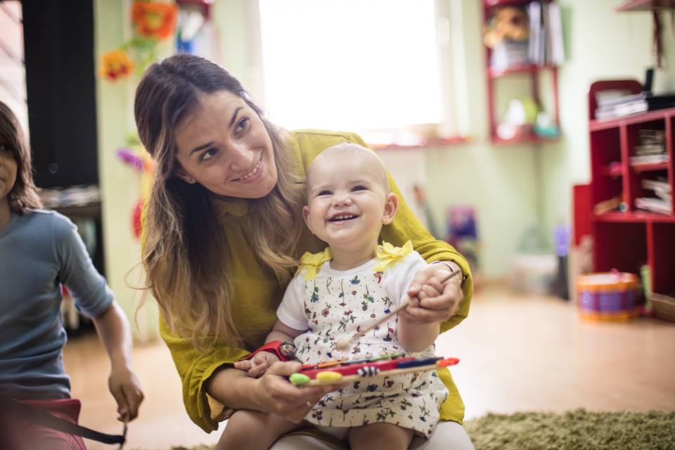 A female early years practitioner helping a young child with a music activity in a nursery