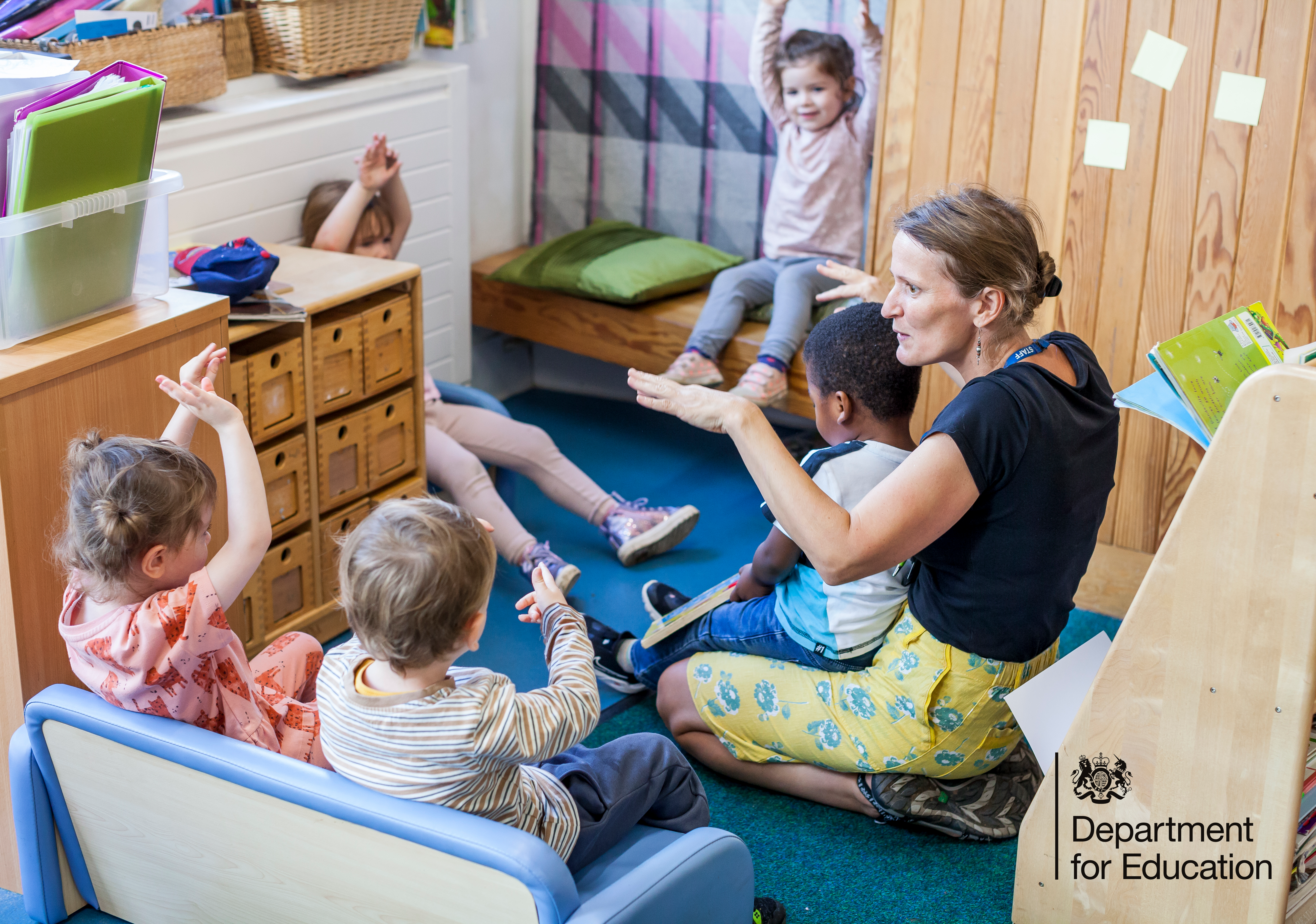 A circle of children copy a practitioner who is showing them how to do hand motions along to a nursery rhyme