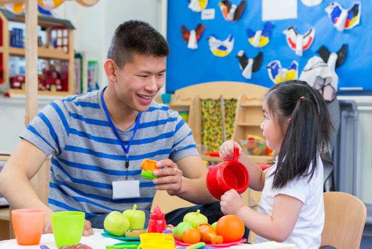 A male early years practitioner doing a food-based activity with a child in a colourful nursery
