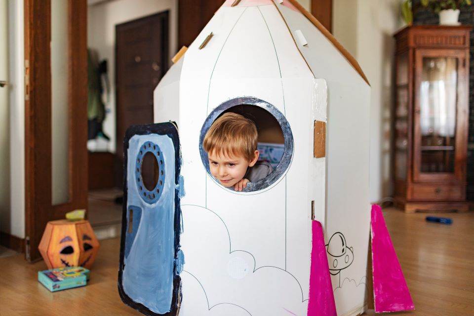 Little boy playing in DIY cardboard rocket.