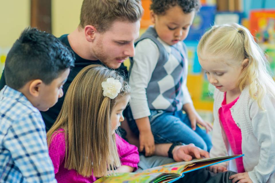 A male early years practitioner reading with a group of young children in a nursery