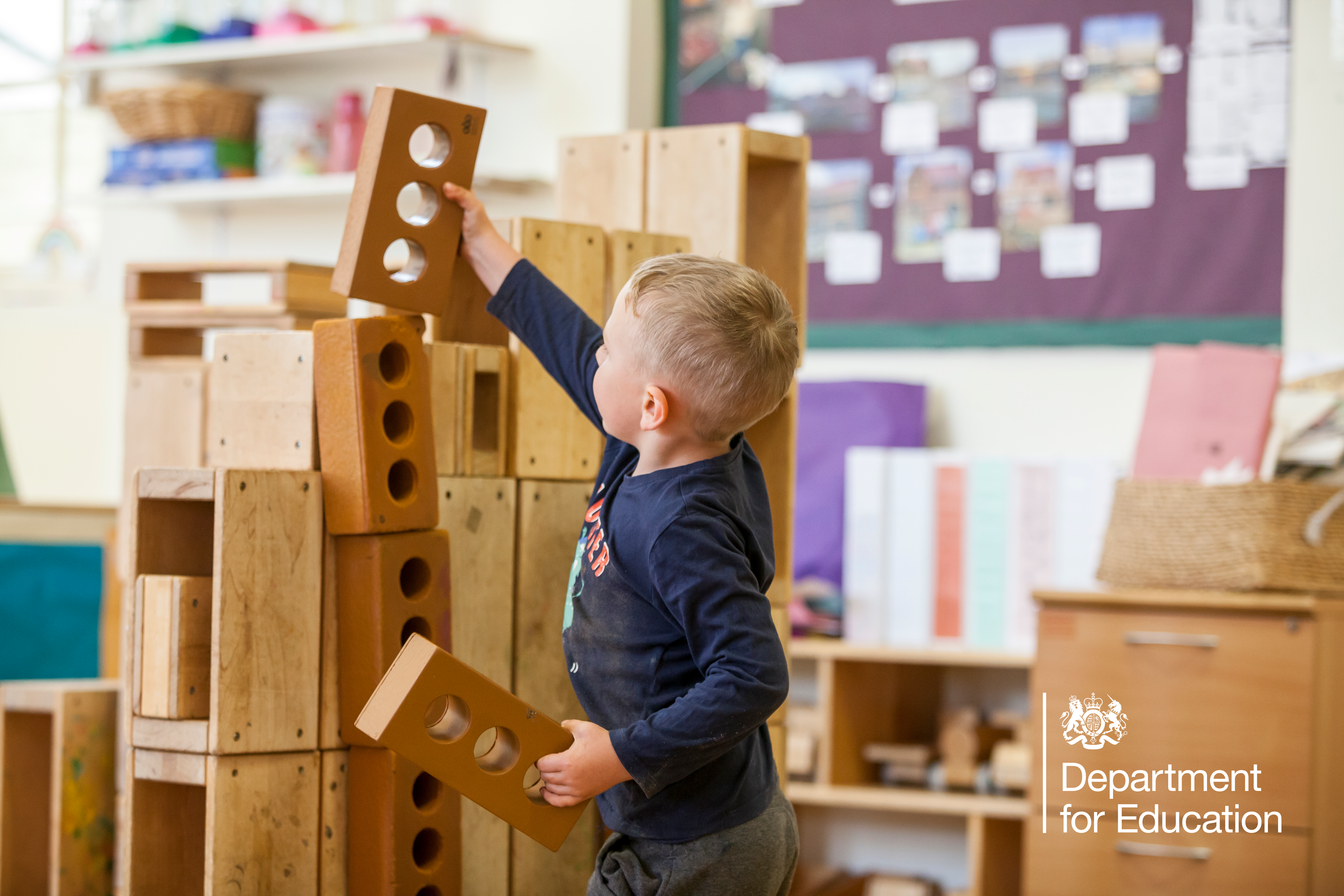 A child reaching up to balance a toy brick on top of a tall tower