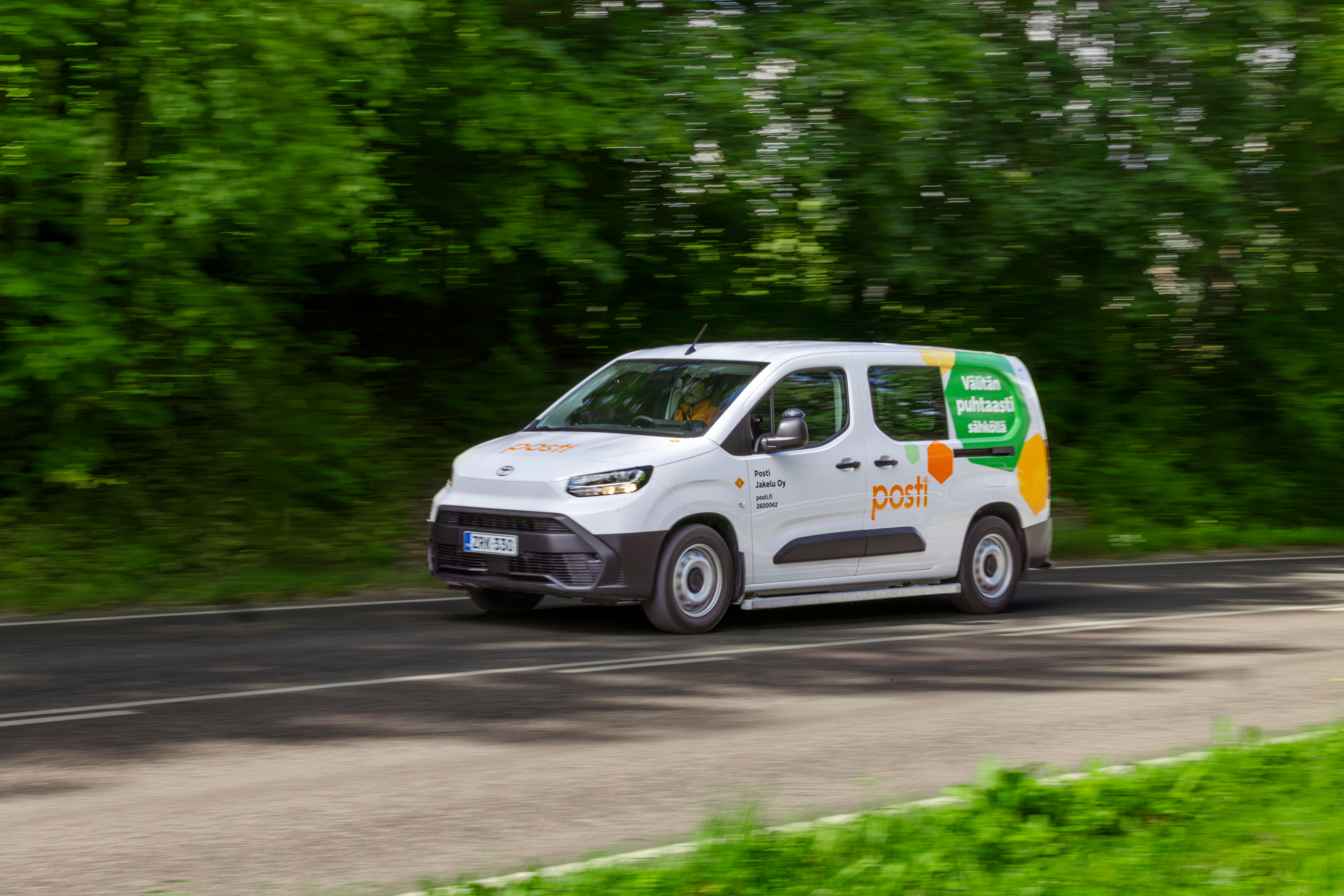 Posti delivery van driving on a road past trees