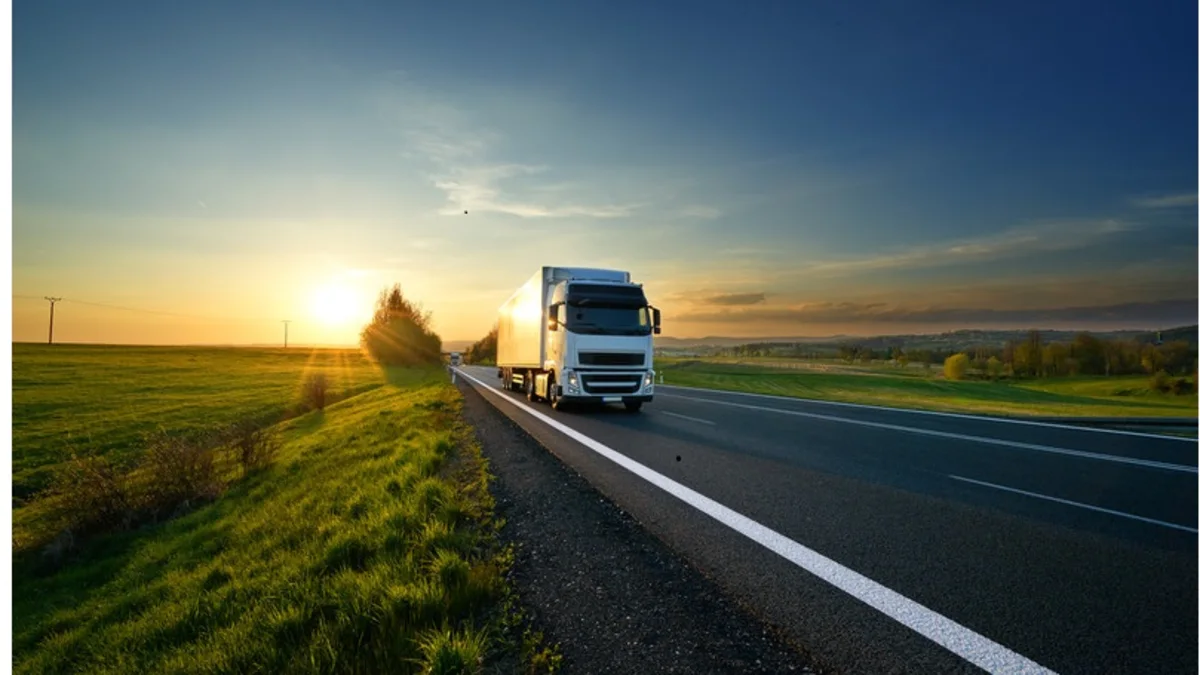 A truck driving a wide road during a sunset.