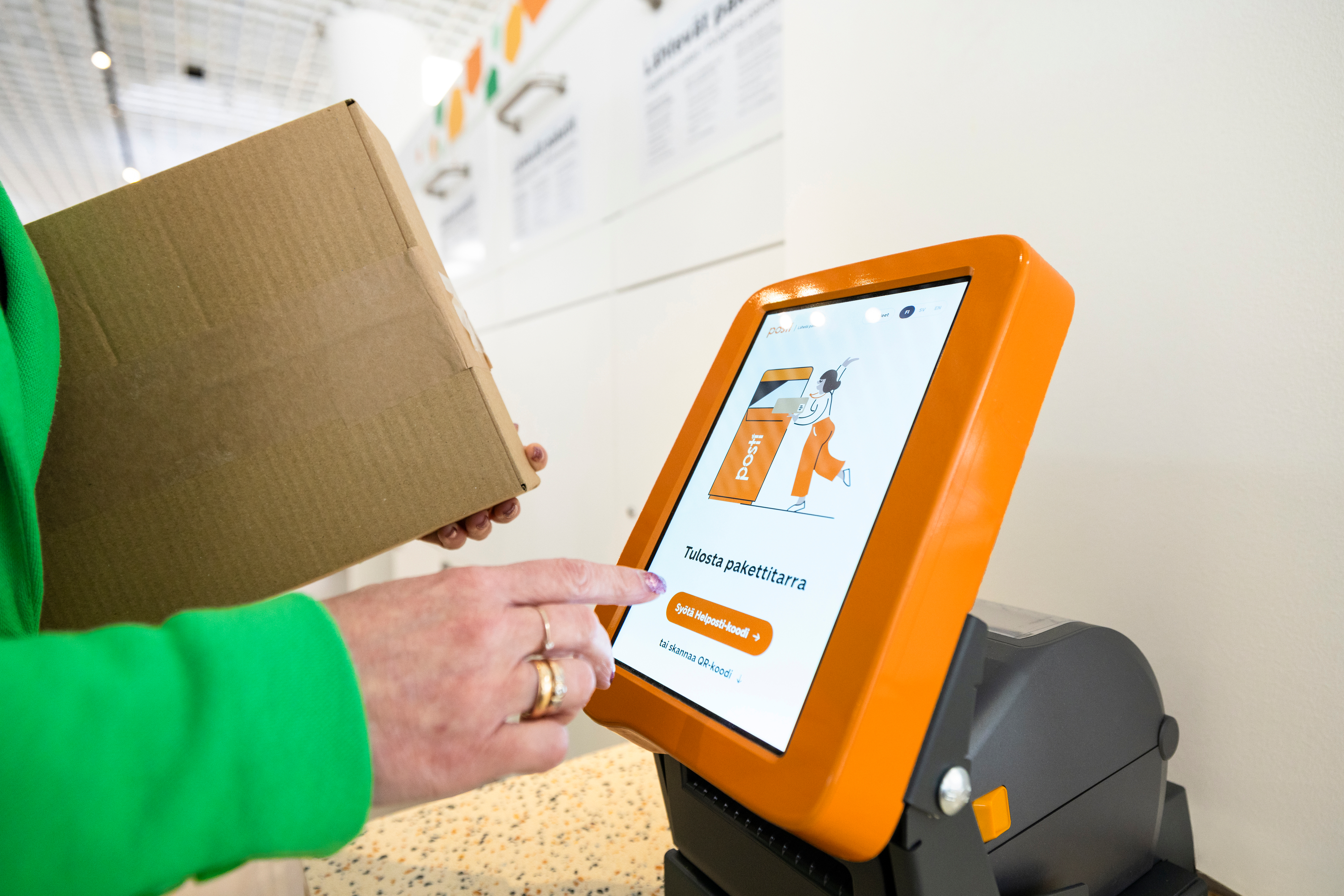 Asiakas tulostaa pakettitarran Postin itsepalvelupisteellä ja pitelee pakettia kädessään.