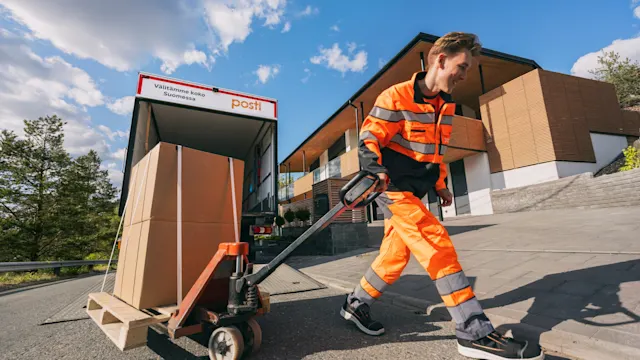 En Postis logistikmedarbetare transporterar ett stort paket med en pallyft.