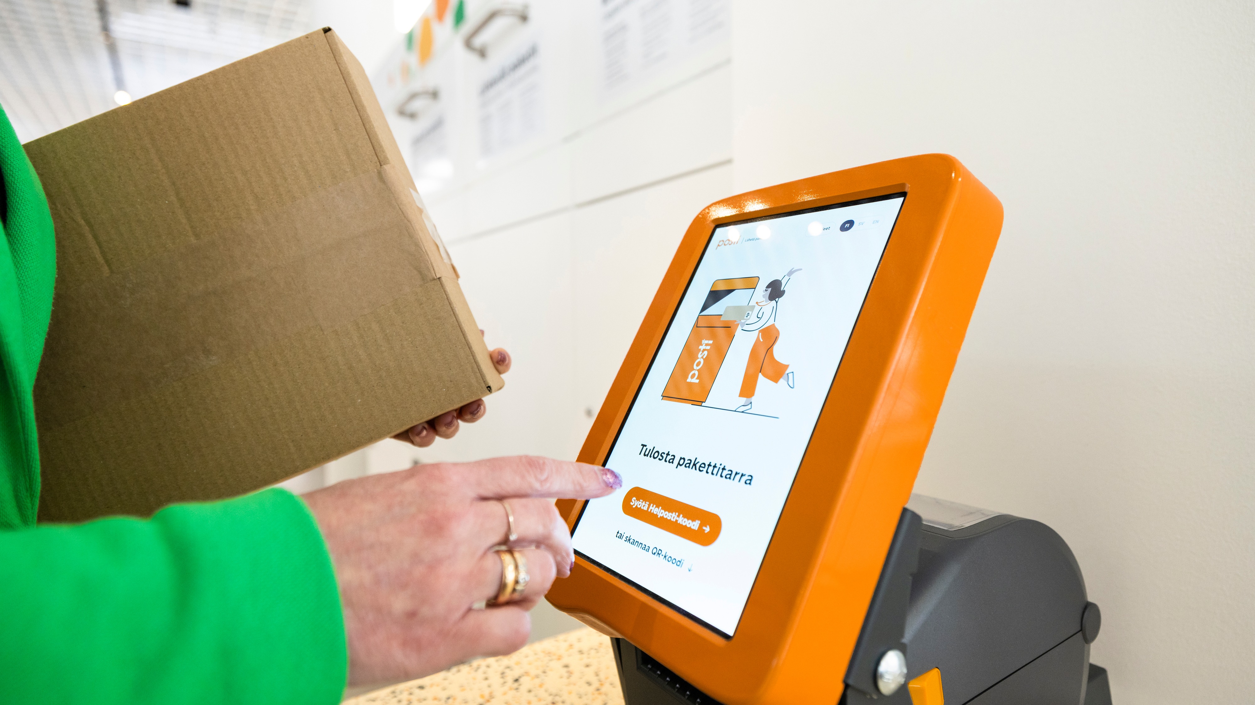 A person sends a parcel at a Posti self-service point using a parcel label printer.