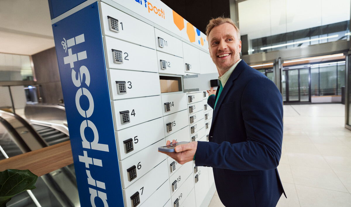 A smiling employee is picking up a package in a SmartPosti warehouse.