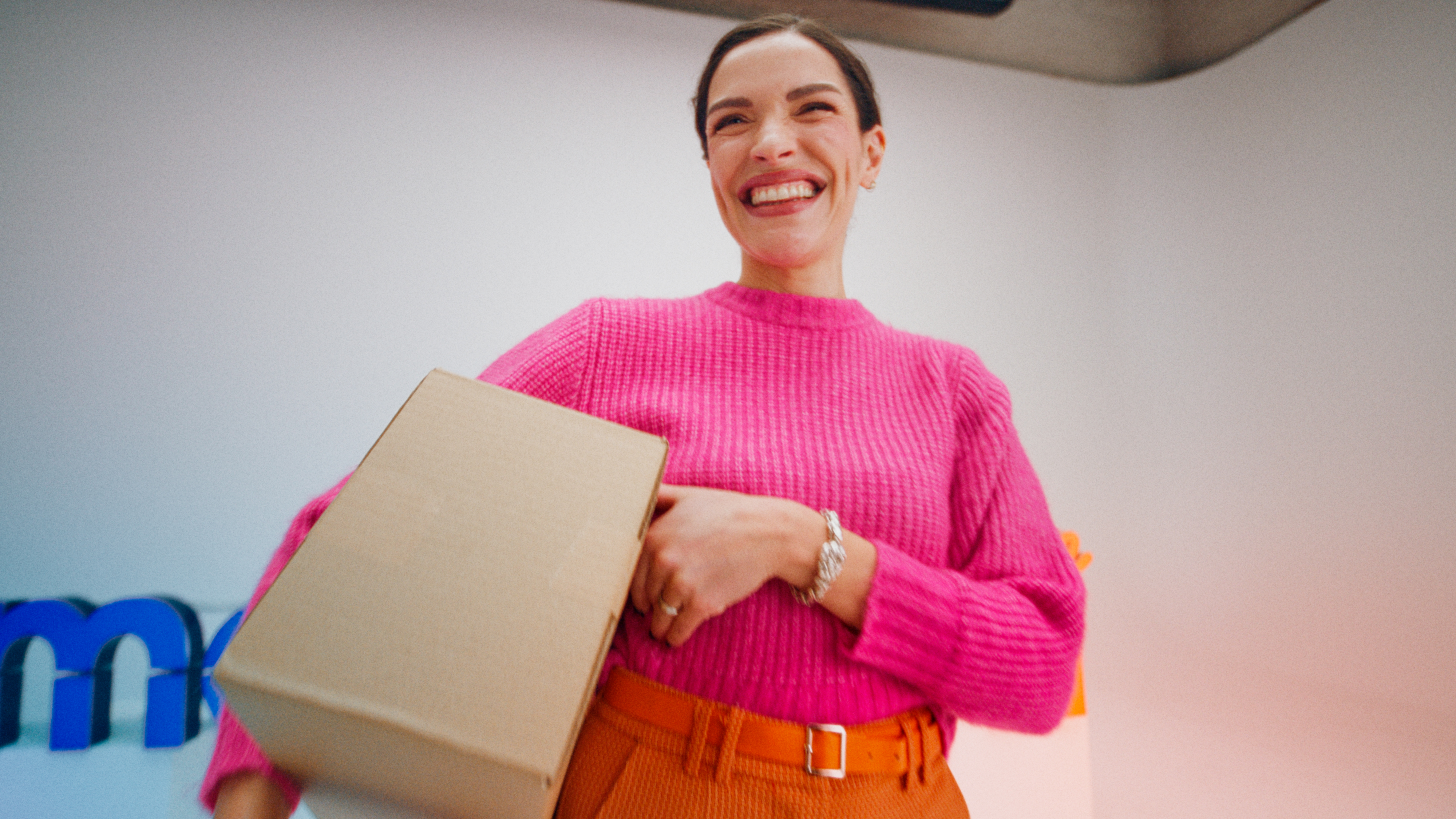 A woman in a pink shirt smiling and carrying a SmartPosti package.