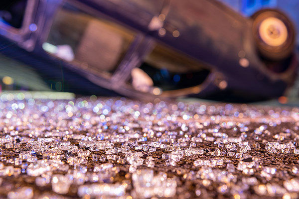 The aftermath of a car accident, with a vehicle overturned and broken glass on the ground.