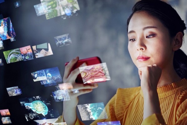 A woman looks at her mobile phone and several images are shown in the background, representing big tech.