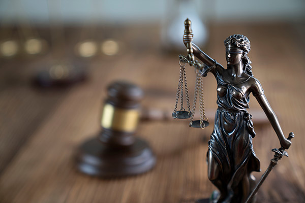 Lady Justice holding scales and a sword, with a judge’s gavel blurred in the background.