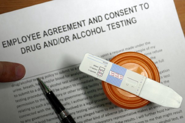 A cannabis drug test sits on top of an employee agreement for a drug test.