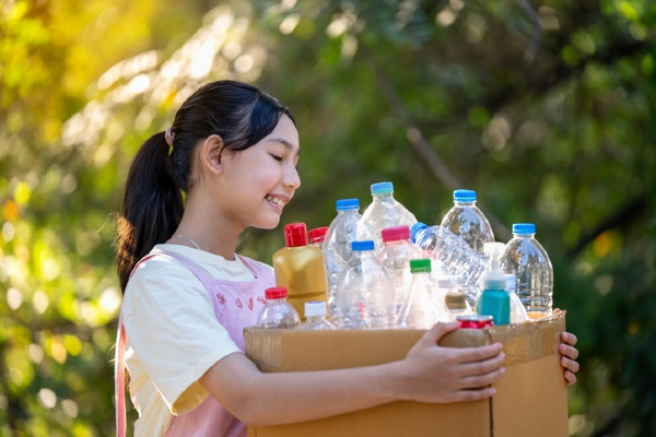 A girl carries a box filled with bottles to recycle.