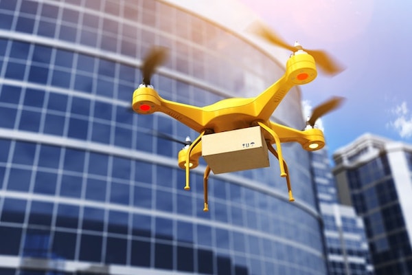 A drone carries a box flies in front of an office building.