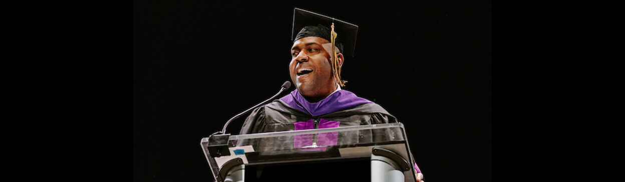 Purdue Global Law School graduate in cap and gown speaking at a podium