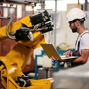 Man standing with laptop in front of machine