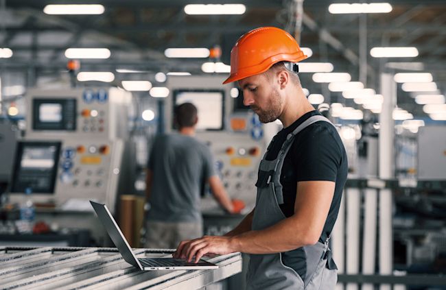 Man standing before laptop in front of a production machinere
