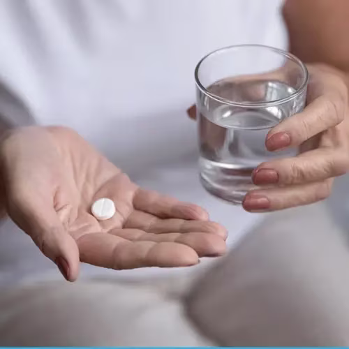 A woman with a pill in one hand and a glass of water in the other.