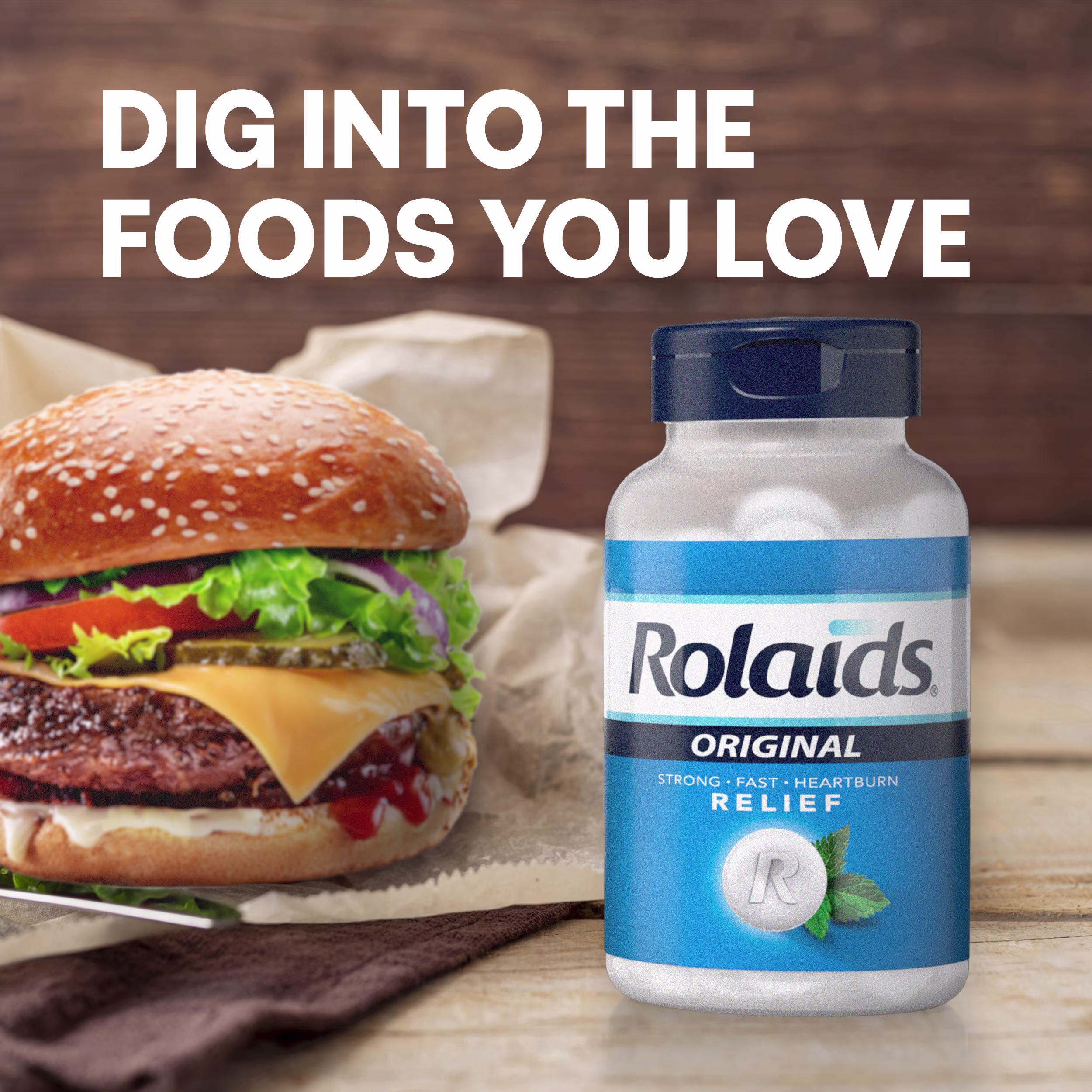 A cheeseburger next to a Rolaids Original bottle on a wooden table with text reading "Dig into the foods you love."