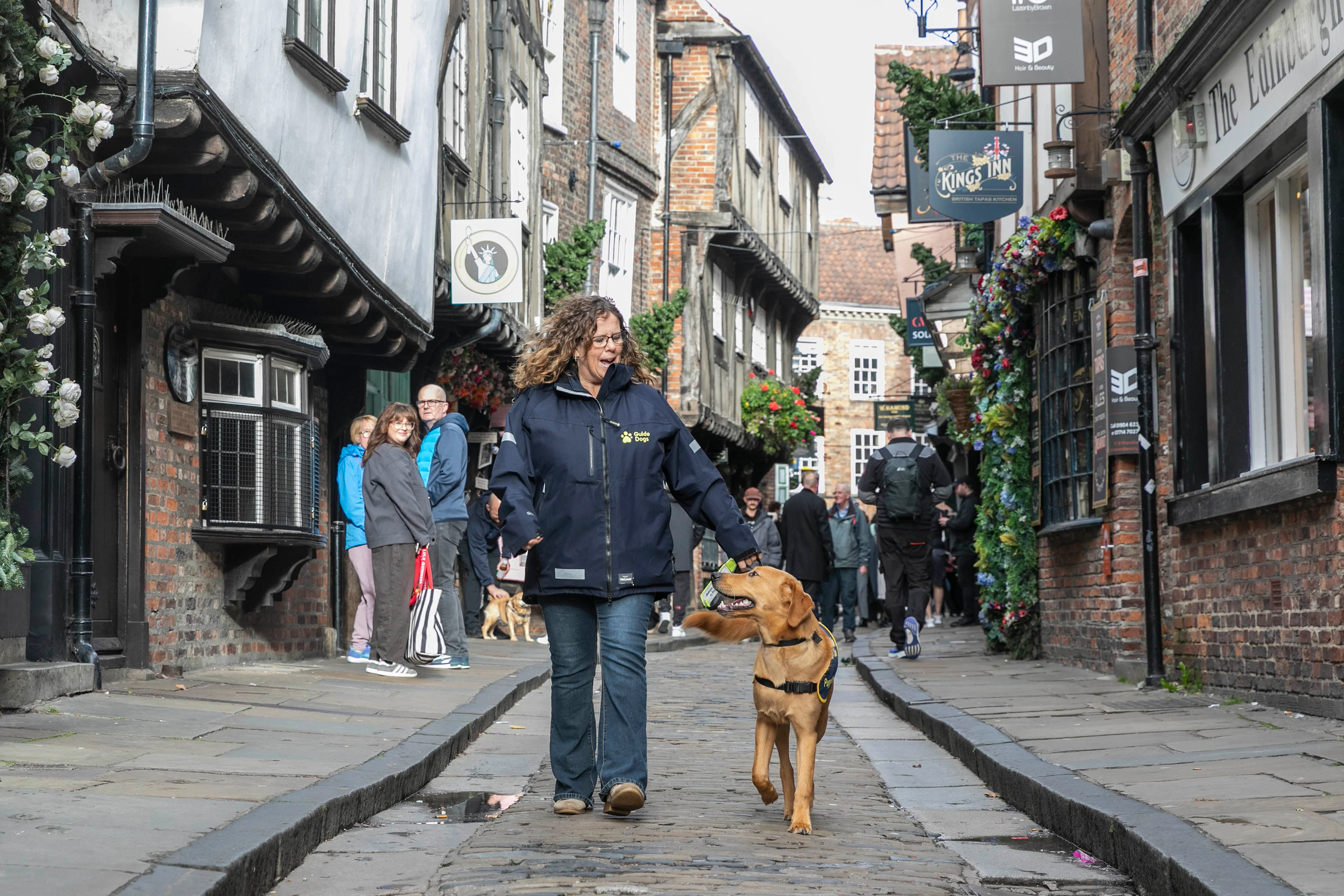Magic the guide dog puppy walks with Wendy Huggins from Guide Dogs along the Shambles in York