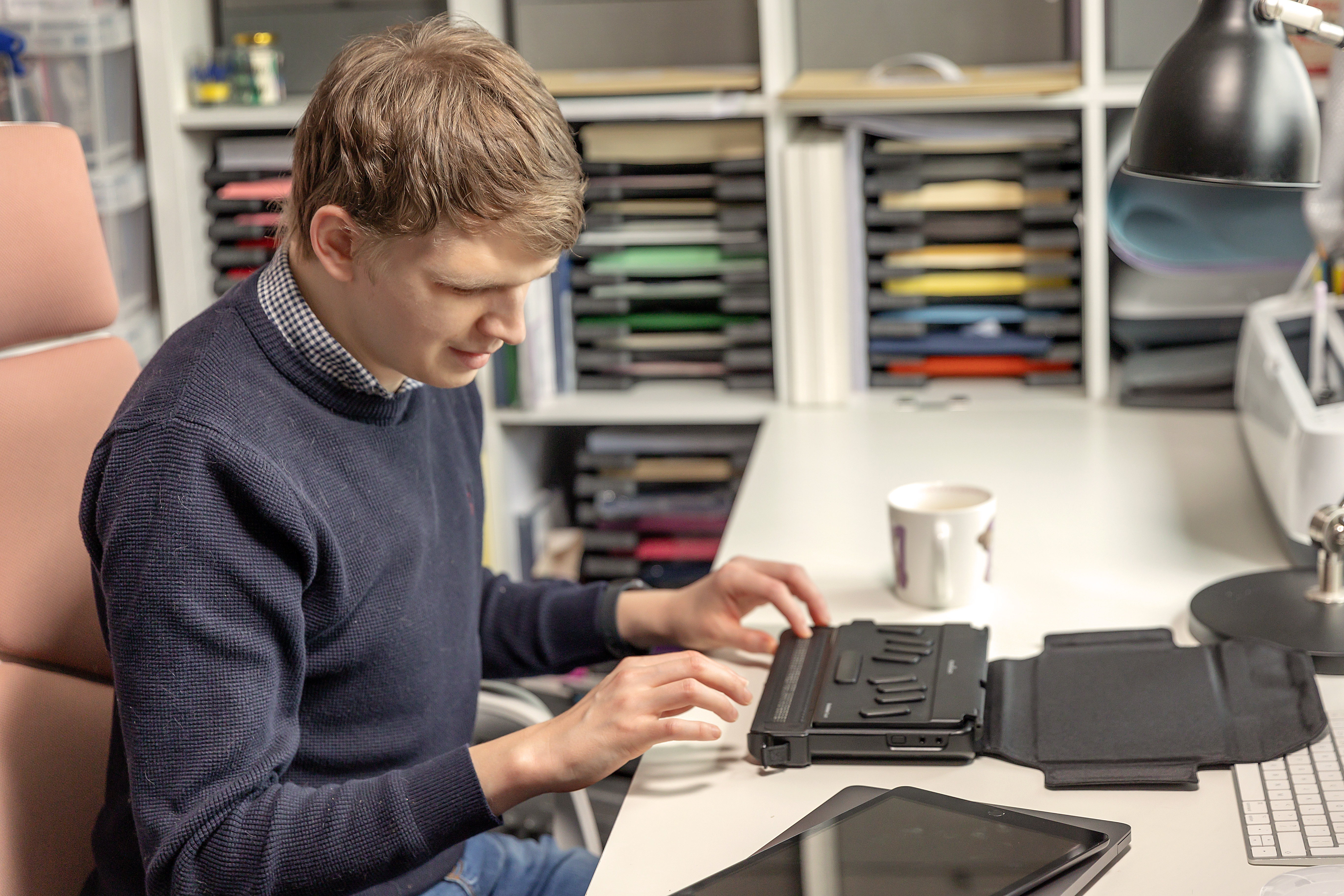 Callum sat at a desk using a braille display.