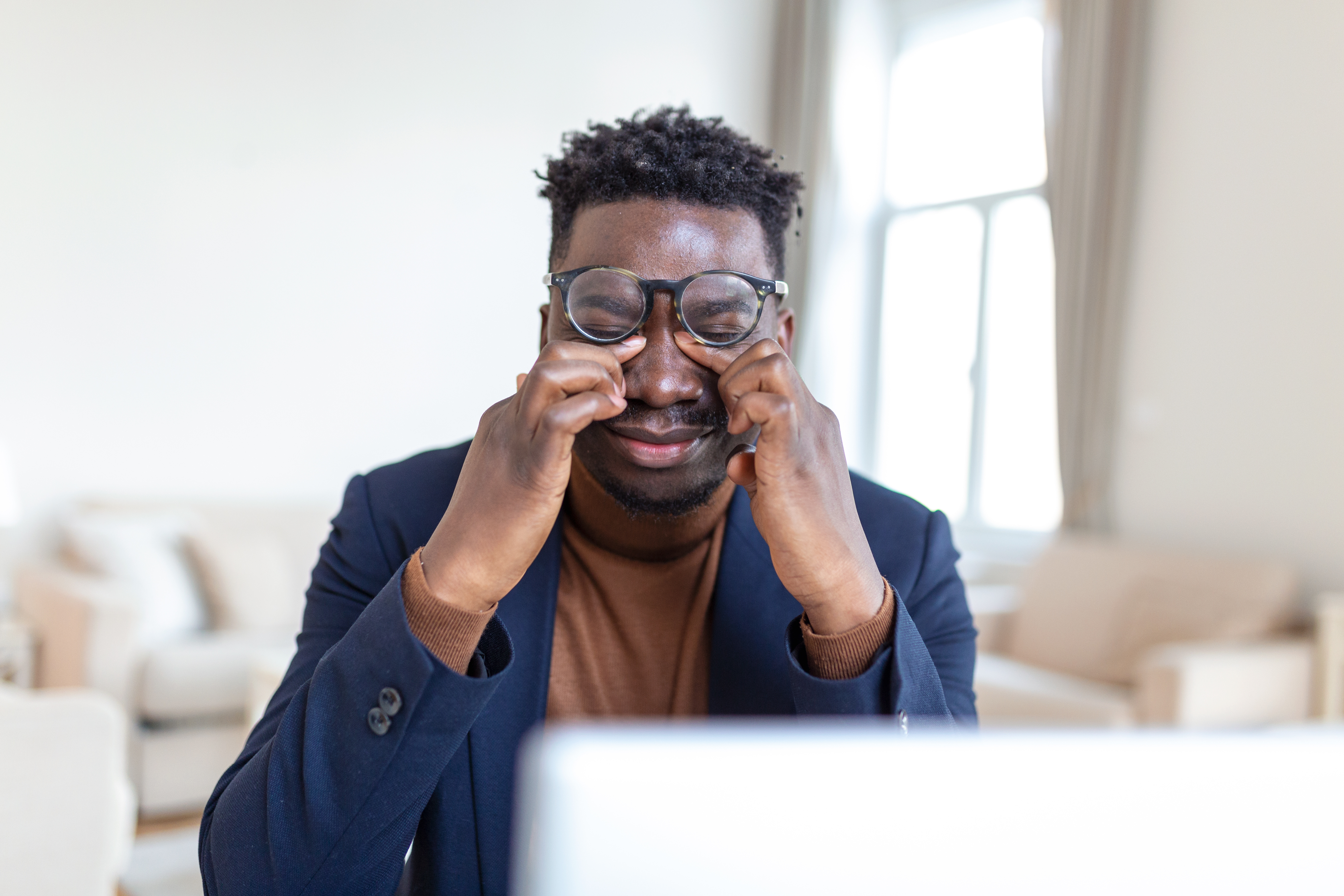 A man rubbing his eyes in front of a laptop