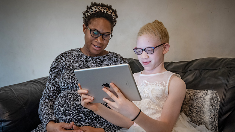 Kamsi sitting on the sofa with her mum, Eremina, reading from an iPad