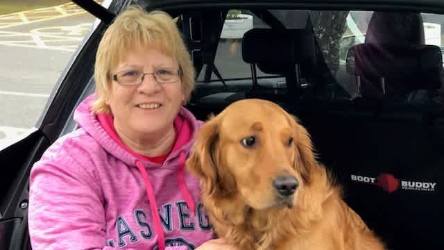 Volunteer Pat Canning is sat in the boot of a car next to a Golden Retriever.