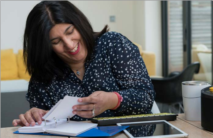 A woman with sight loss sat at a desk, using accessible technology.