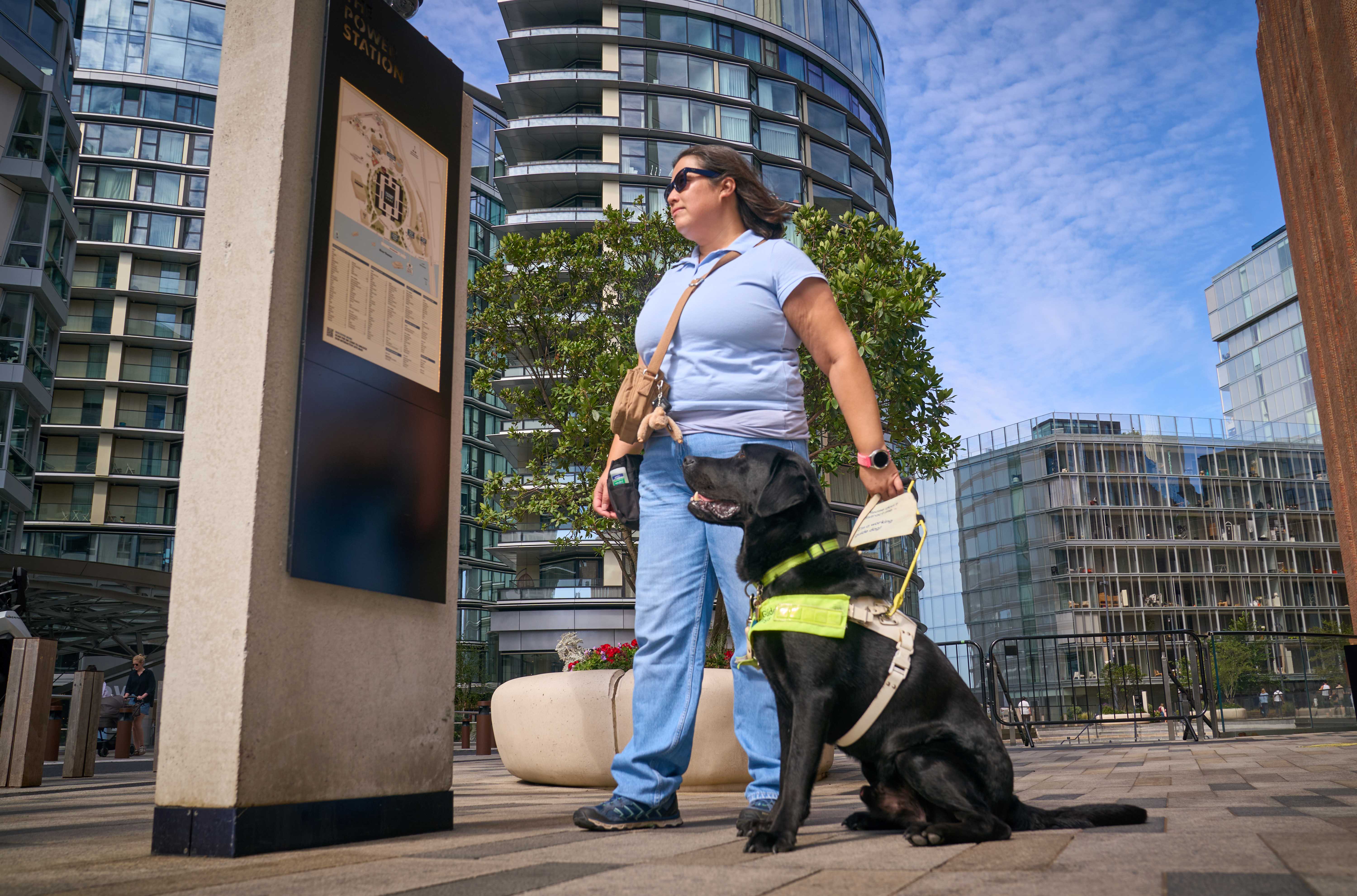 Black Lab guide dog Dalby sits next to his owner Kimberley and looks at a board displaying a map of some shops