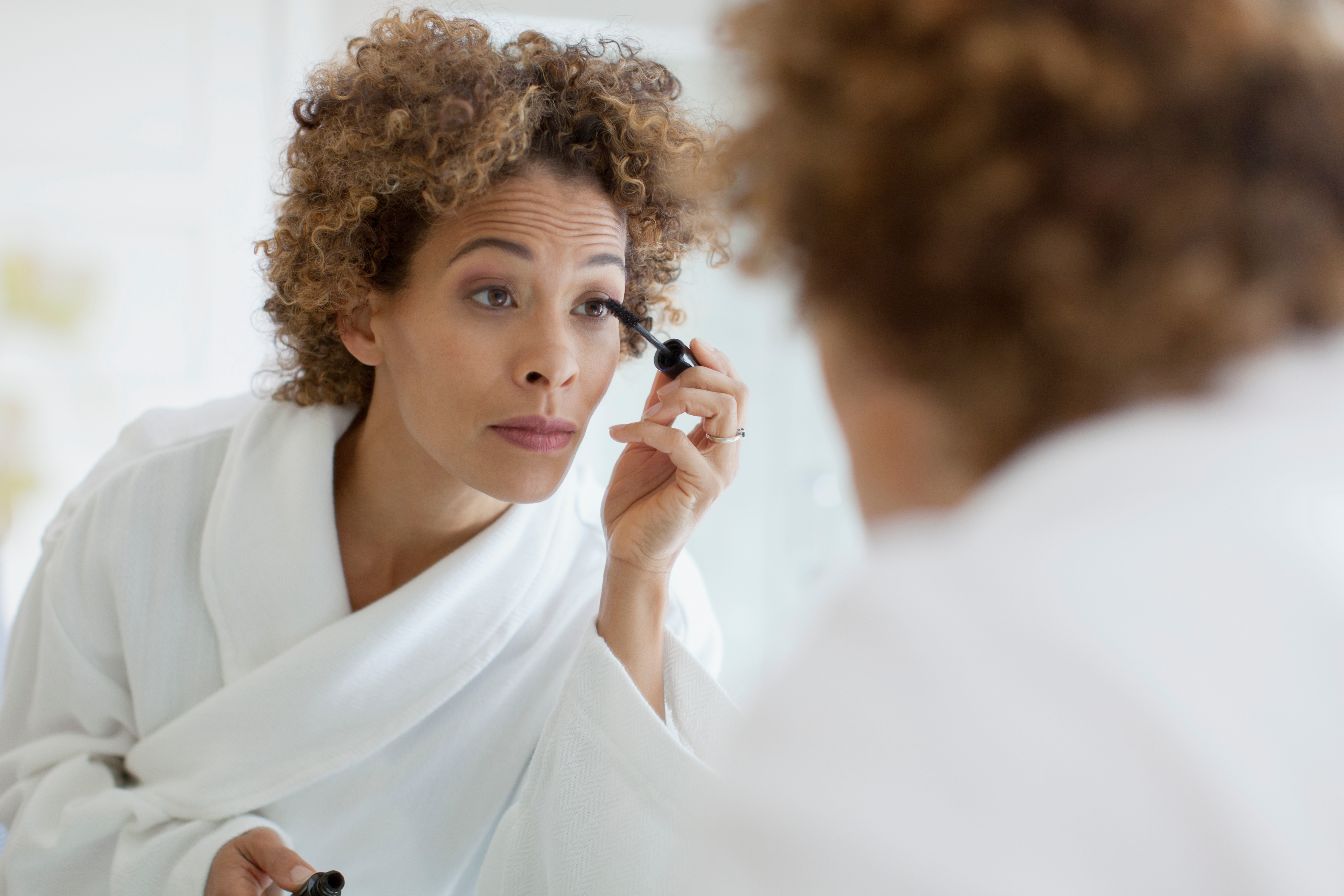 A woman applying mascara in front of a mirror