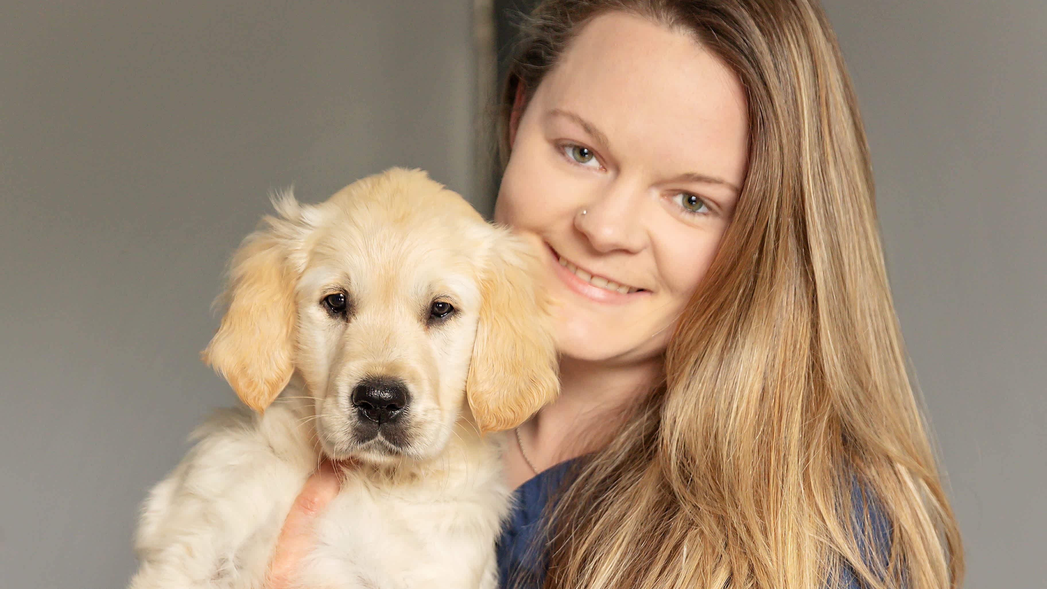 Becky Hunt holds a golden retriever puppy in her arms - they are both looking at the camera