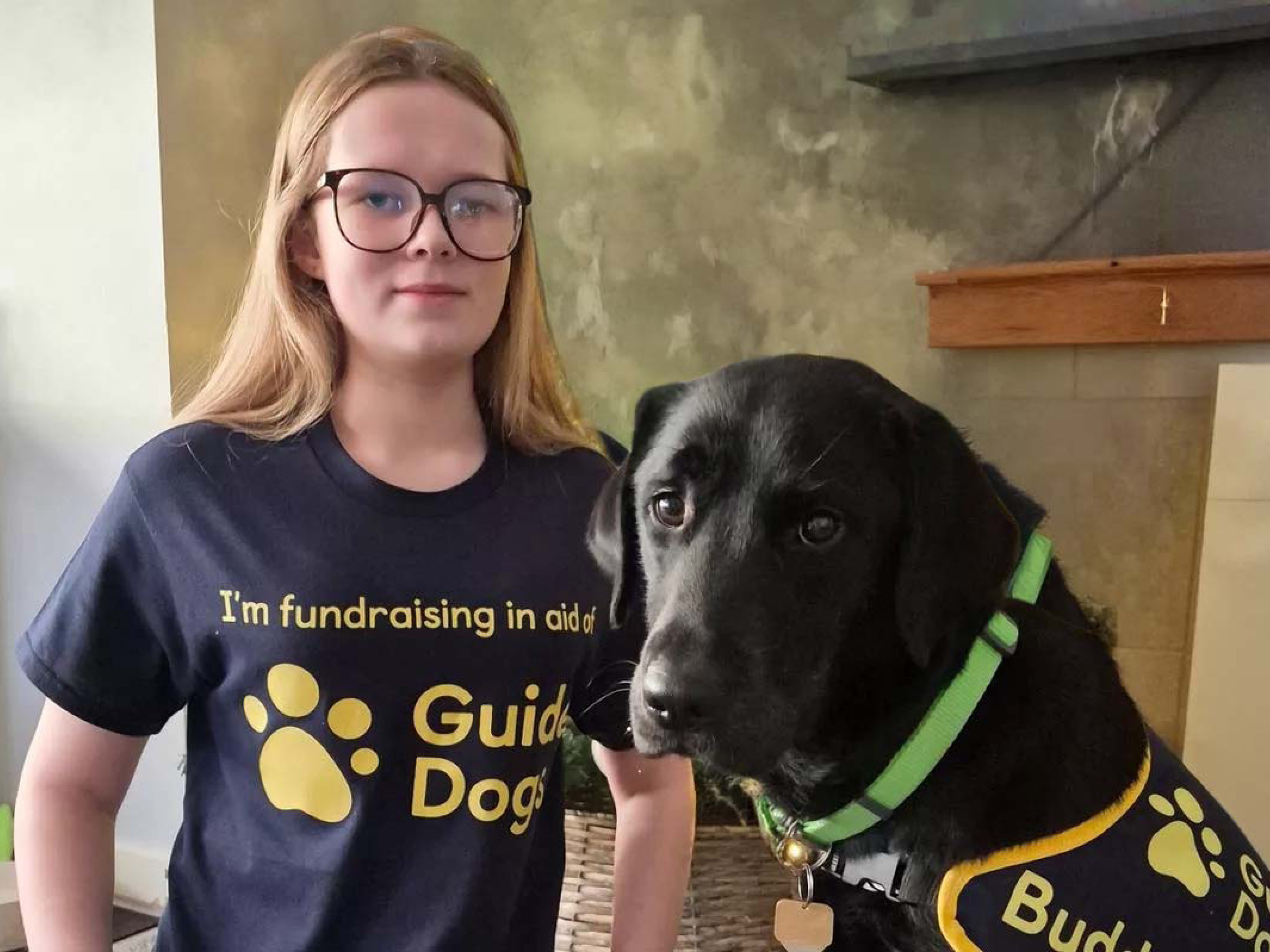 A young fundraiser called Aniyah kneels down next to a black labrador retriever guide dog.
