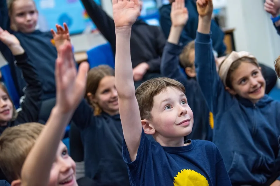 A group of school pupils raising their hands at an assembly. 
