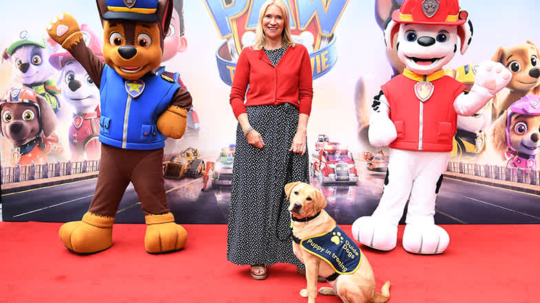 Guide dog puppy in training Flash with Puppy Raise Melanie Nevel on the red carpet with Paw Patrol characters Chase (left) and Marshall.