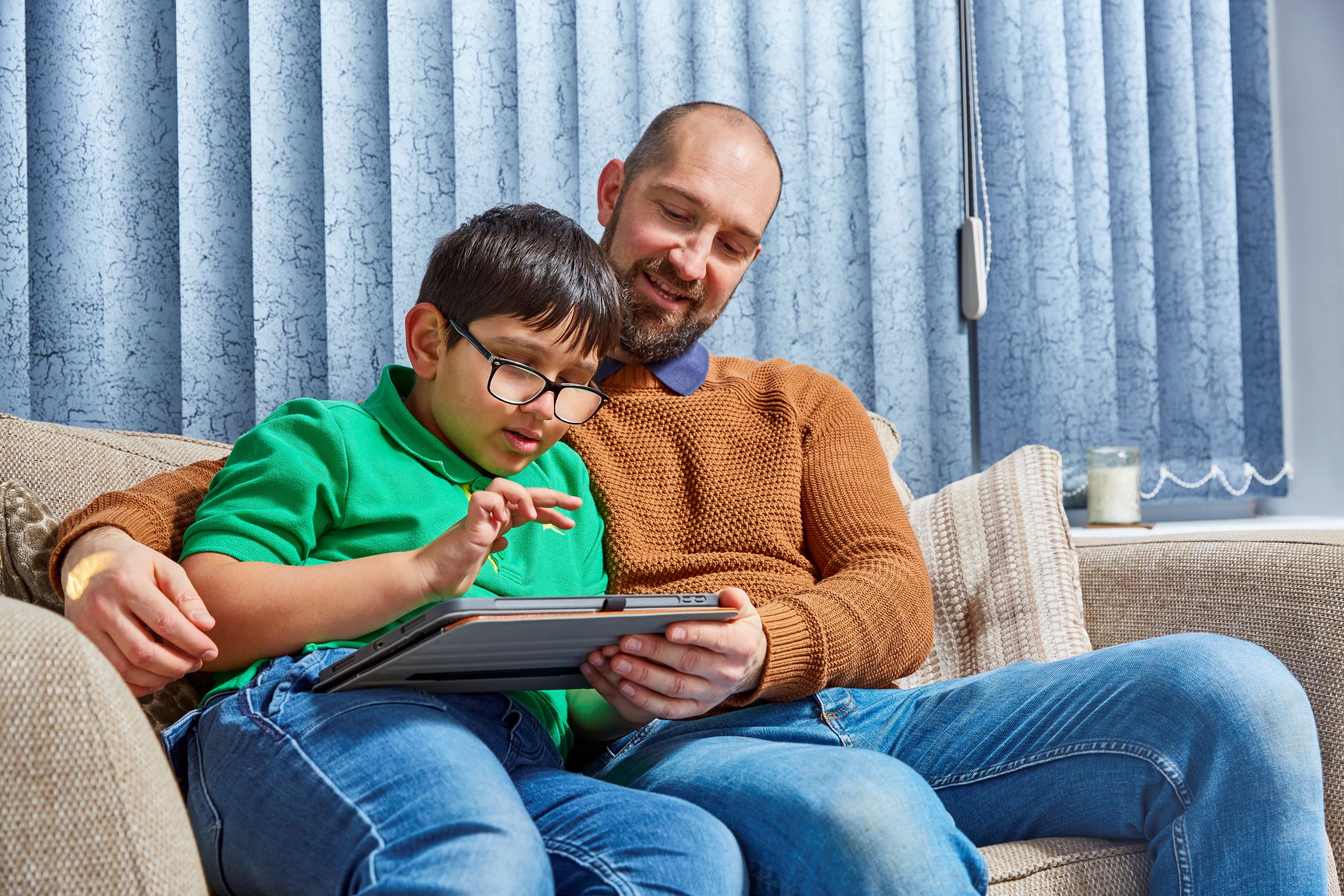 Dad Phil sitting with son Teddy on the sofa as they use a Tech for All iPad