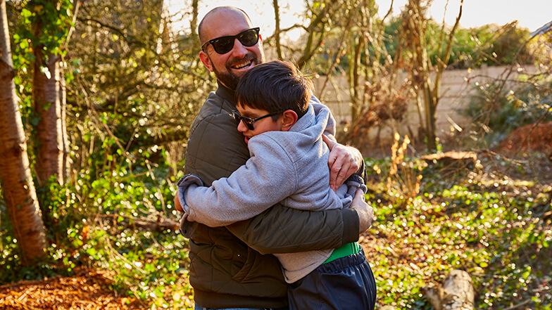 Dad Phil hugging his young son Teddy in a sunny woodland location