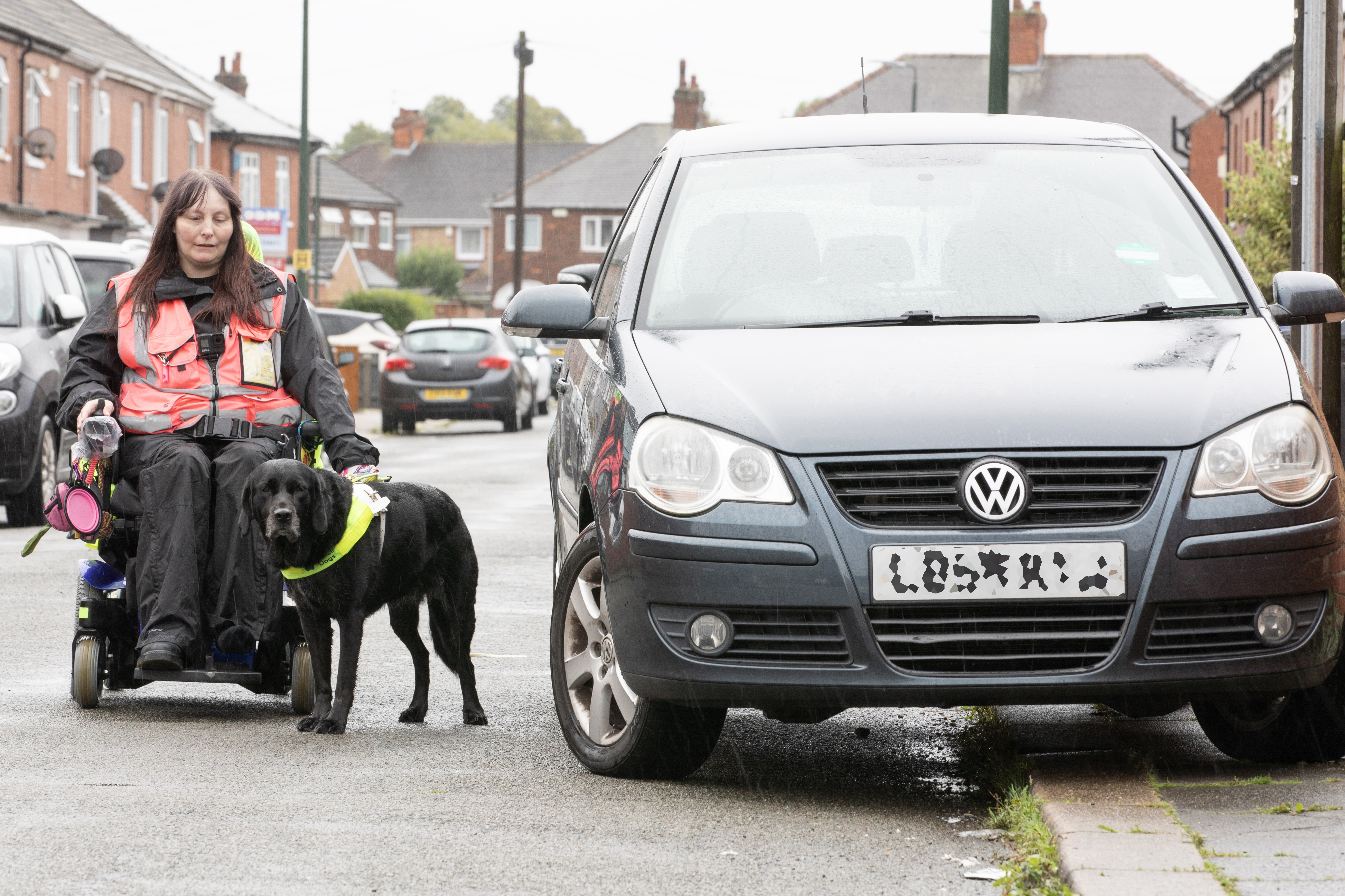 Power chair user Julie Pilsworth and her guide dog Maeve encountering pavement parking and having to pass a car in the road. 