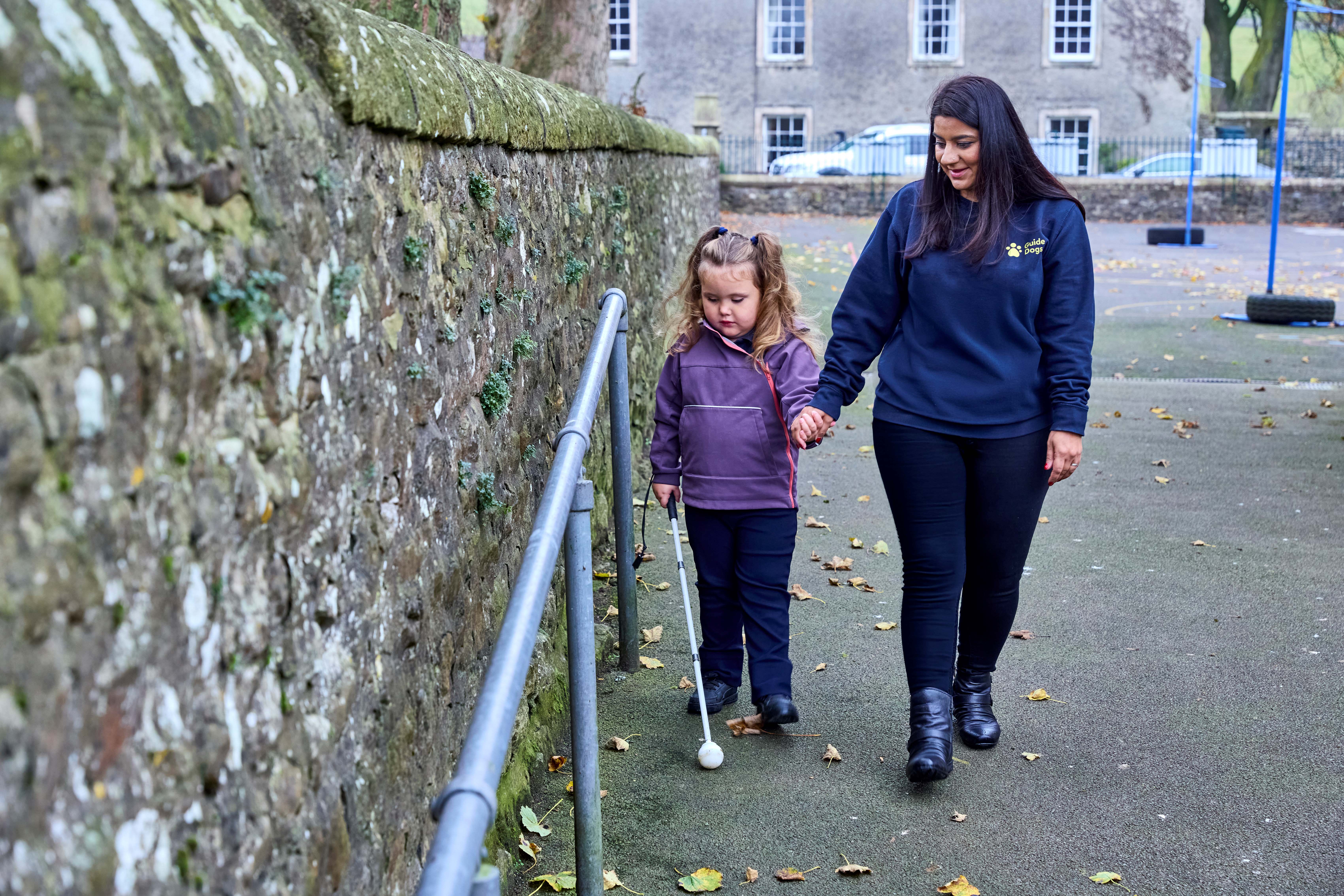 Habilitation Specialist Sunita walks hand in hand with four-year-old Mabel who uses her cane to identify obstacles on a path.