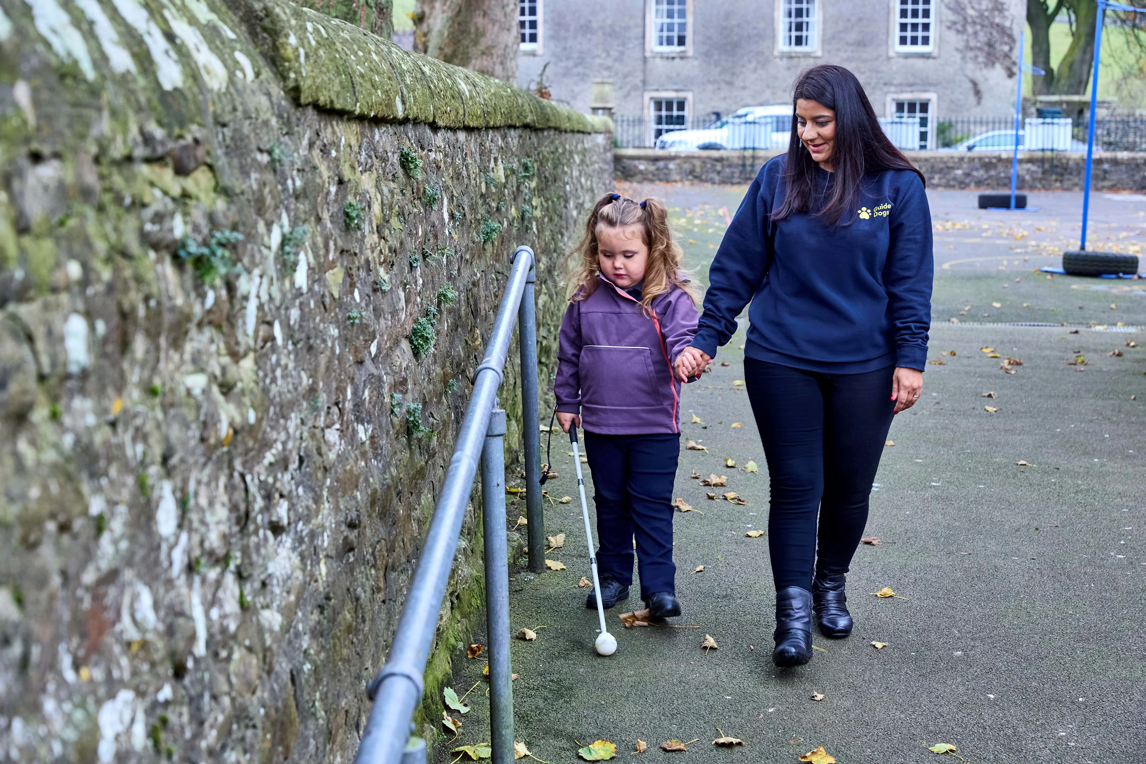 Habilitation Specialist Sunita walks hand in hand with four-year-old Mabel who uses her cane to identify obstacles on a path.