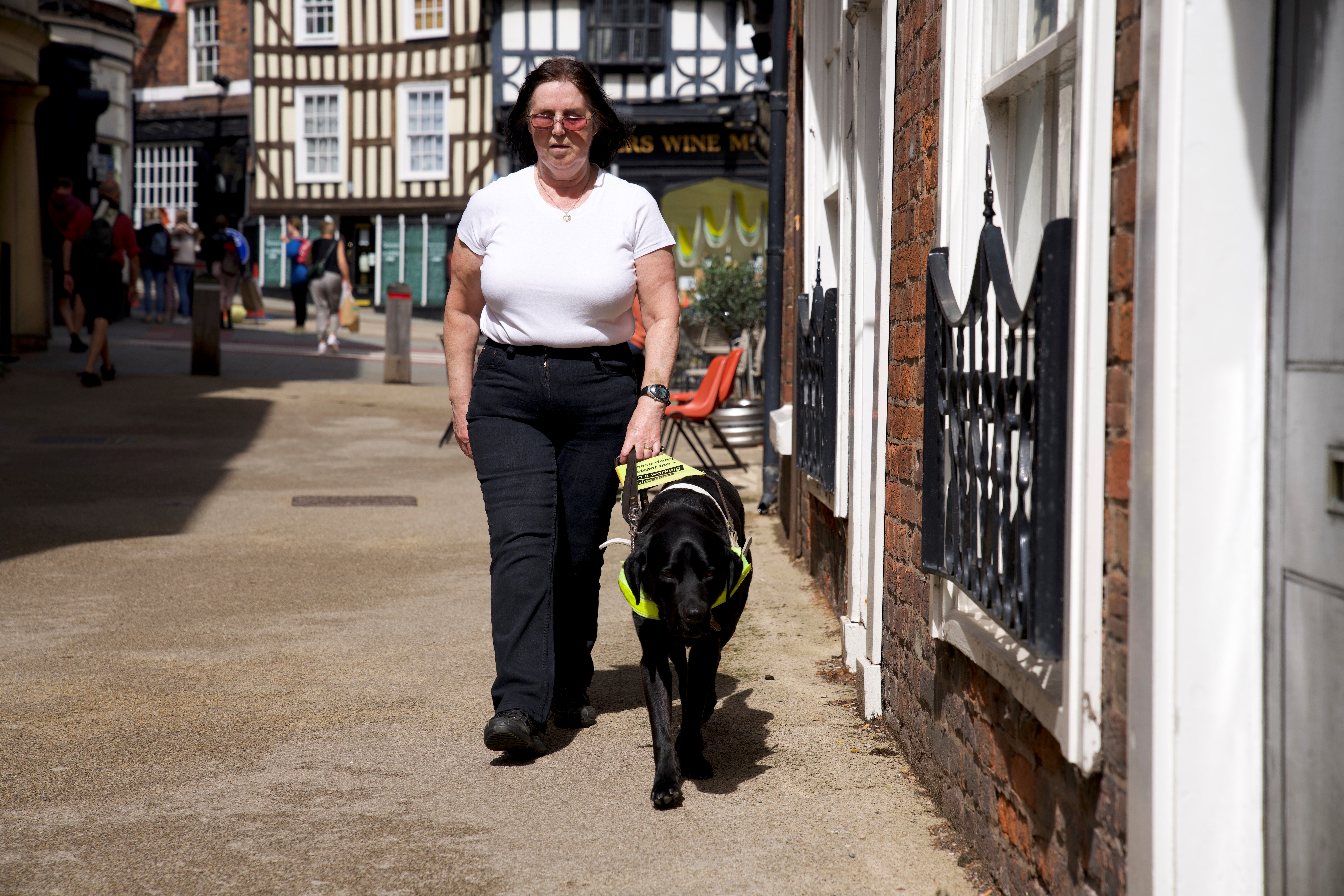 Lindsey is walking down a street being guided by Leyland, a black Labrador