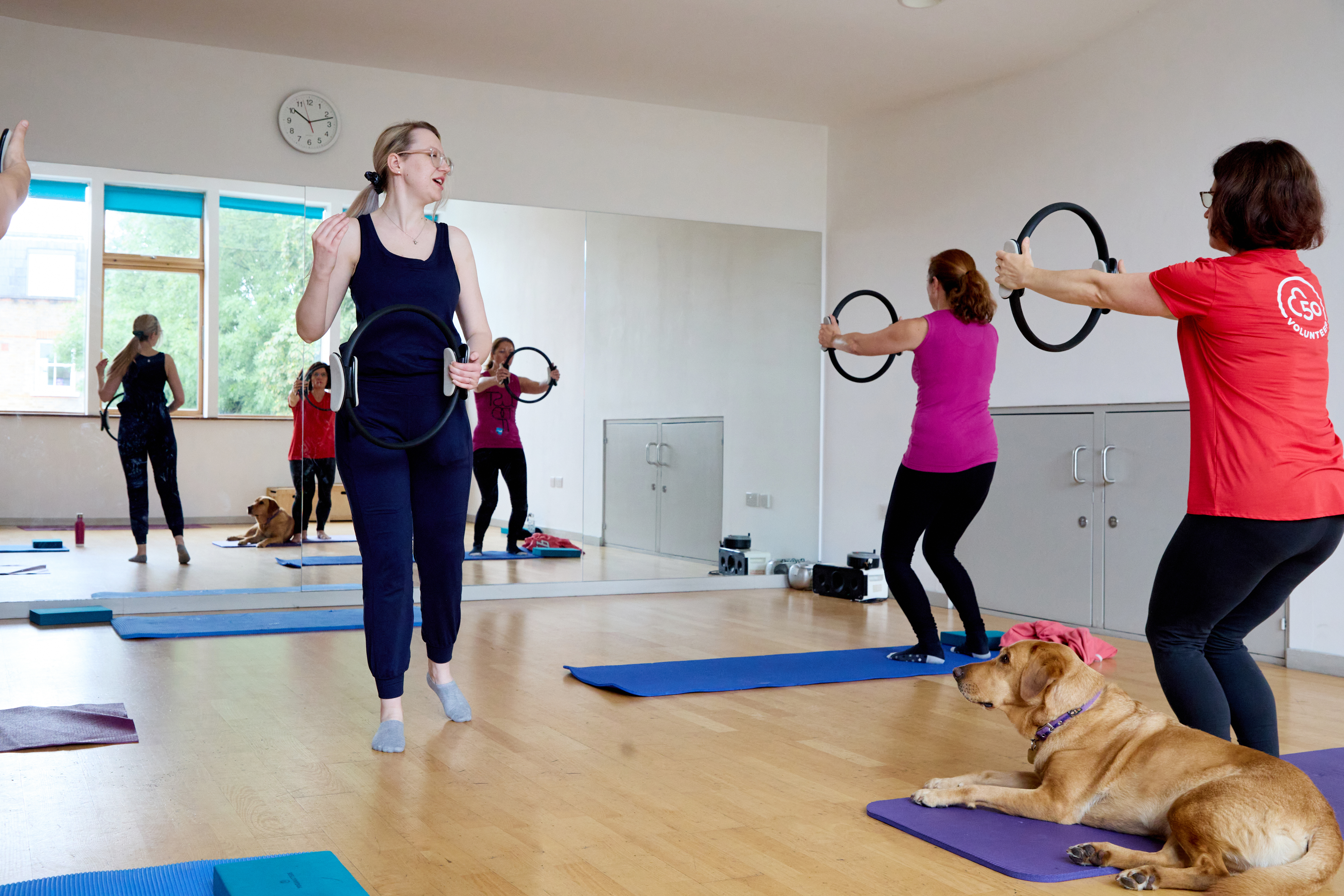 Emma leads a pilates class whilst Archie her guide dog sits on a yoga mat.