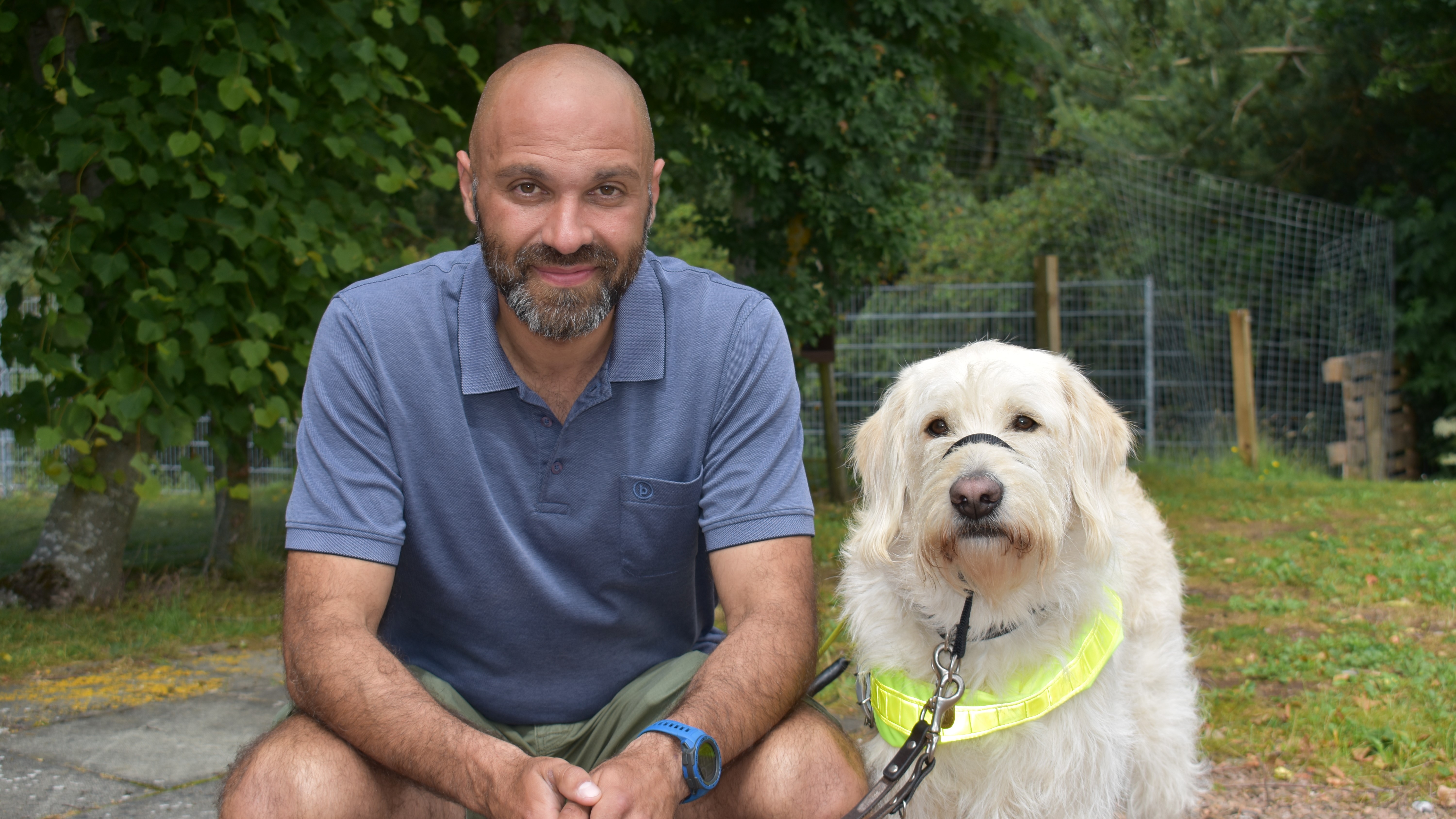 Guide Dog Mobility Specialist Paco sits next to cream Labradoodle Piran, who has a shaggy coat and wears a florescent guide dog harness